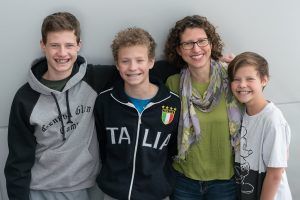 A woman and three boys are posing for a picture together . one of the boys is wearing a jacket that says italia.