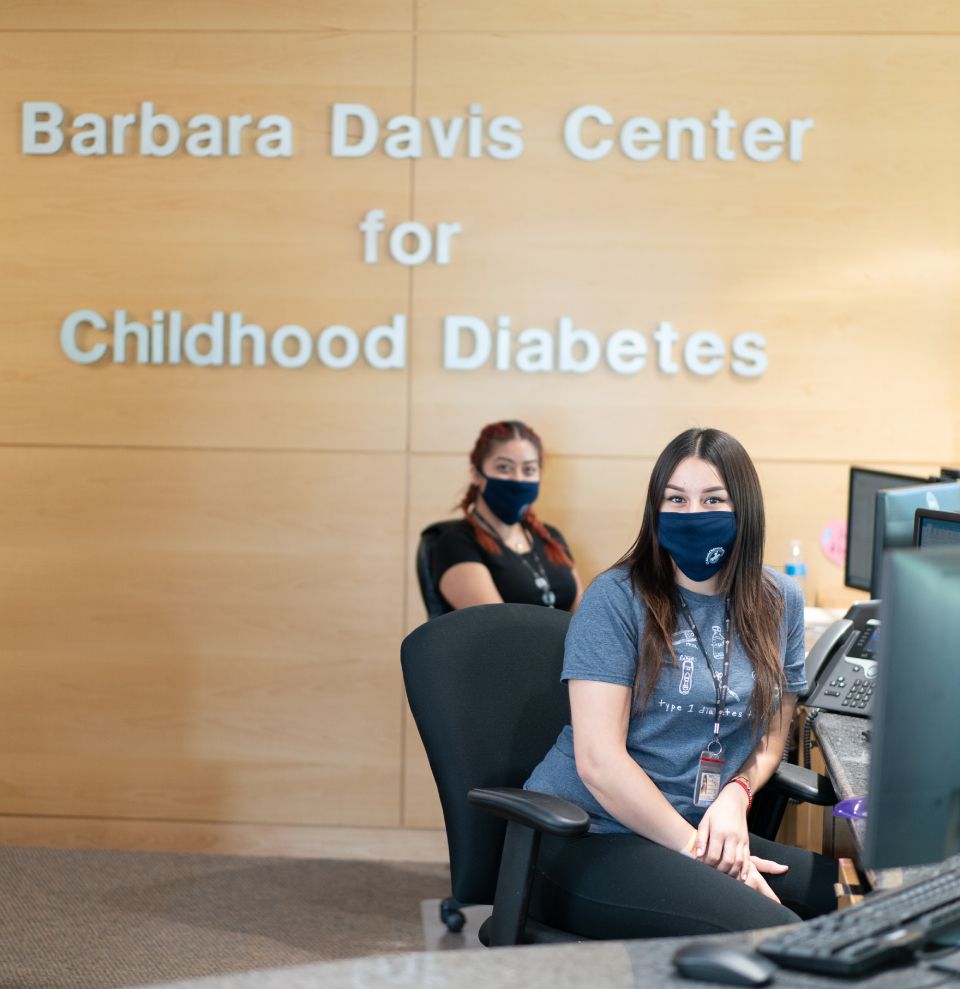 Two Barbara Davis Center staffers sitting at the check-in desk with masks on.