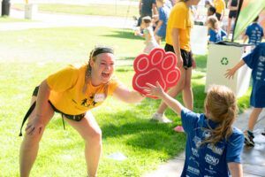 A woman in a yellow shirt is giving a paw print frisbee to a little girl.