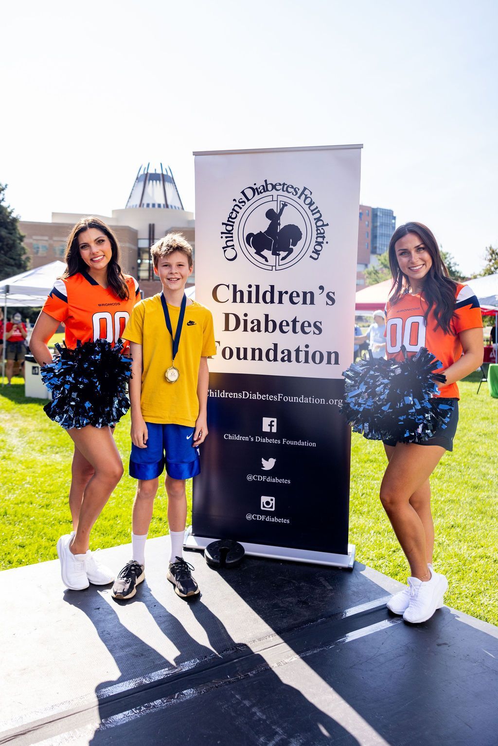 Two cheerleaders and a boy are standing in front of a children 's diabetes foundation sign.
