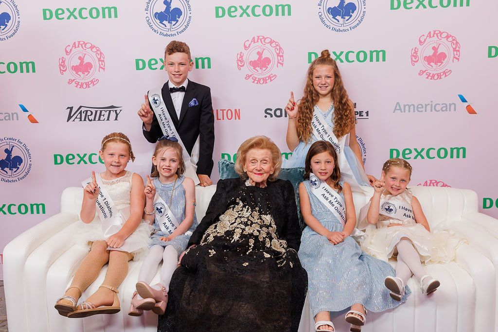 CDF founder Barbara Davis posing on red carpet with six young CDF advocates.