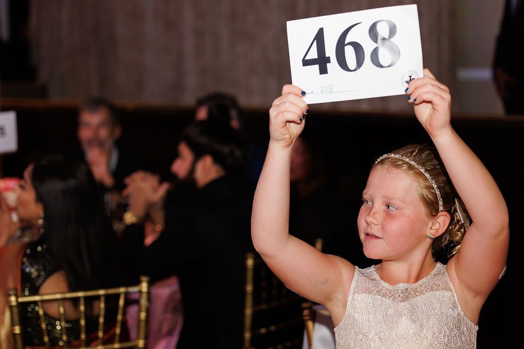 Young girl holding up her paddle number to bid during the live auction.