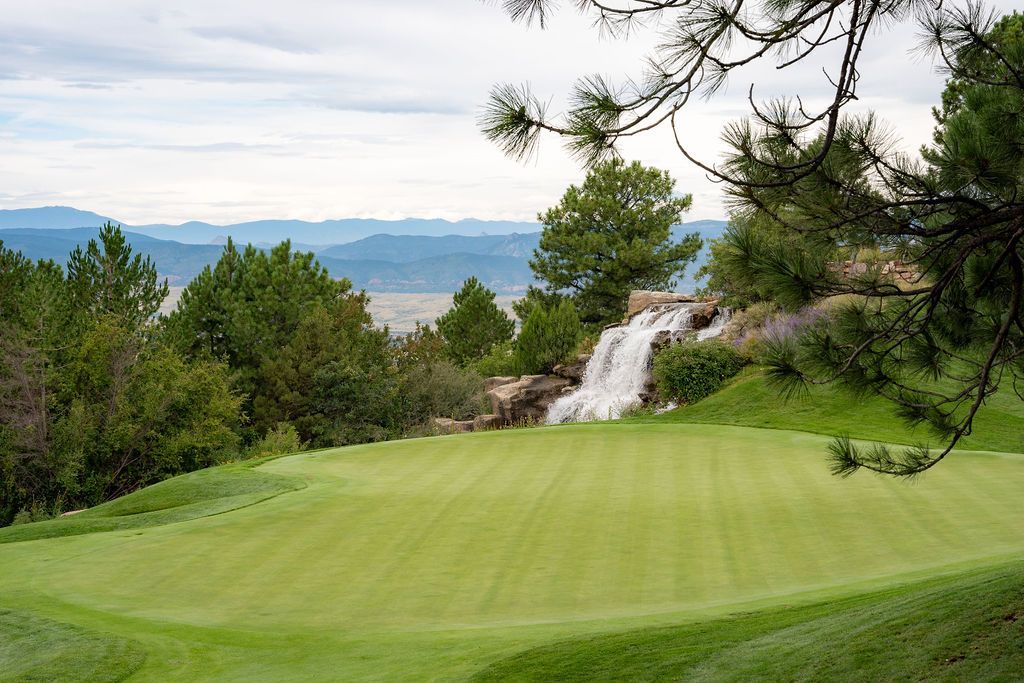 View of golf green with waterfall, trees, and mountains in the background.
