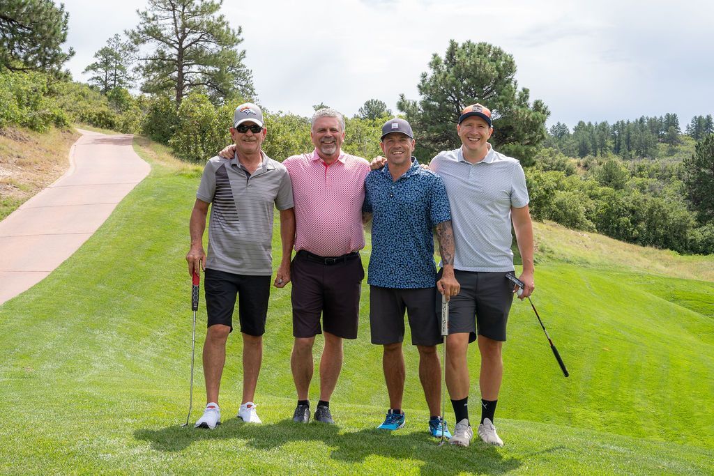 Four male golfers smiling together on the fairway on a sunny day.