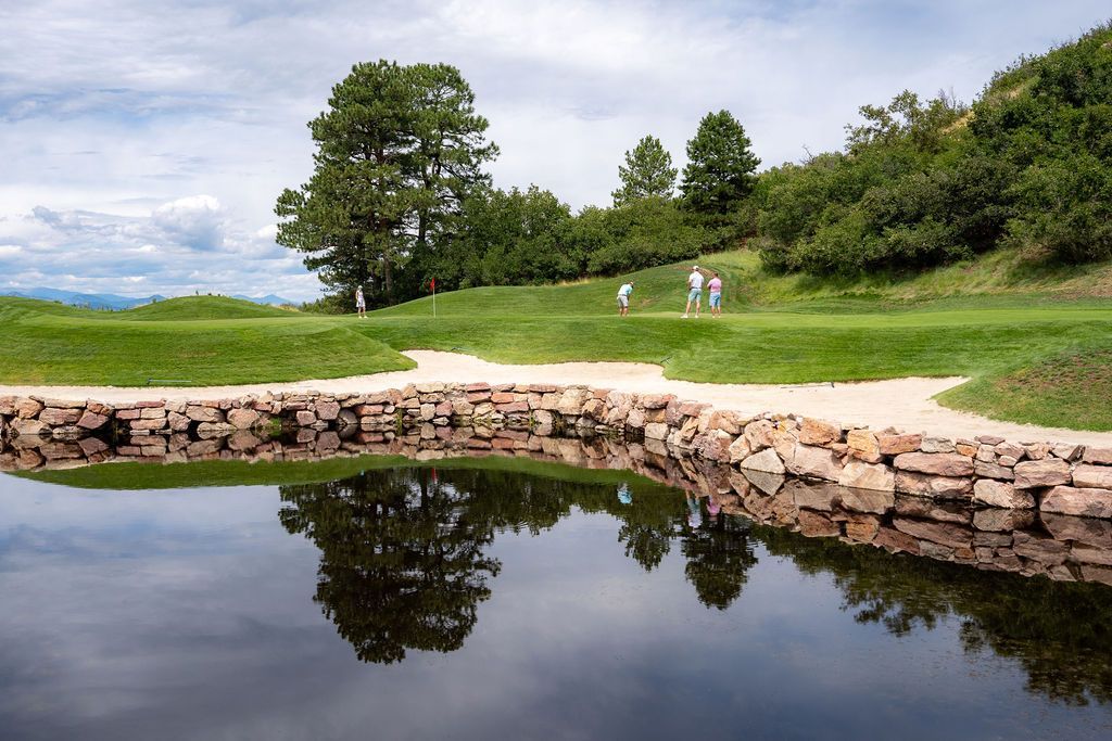 A couple of people are walking on a golf course next to a pond.