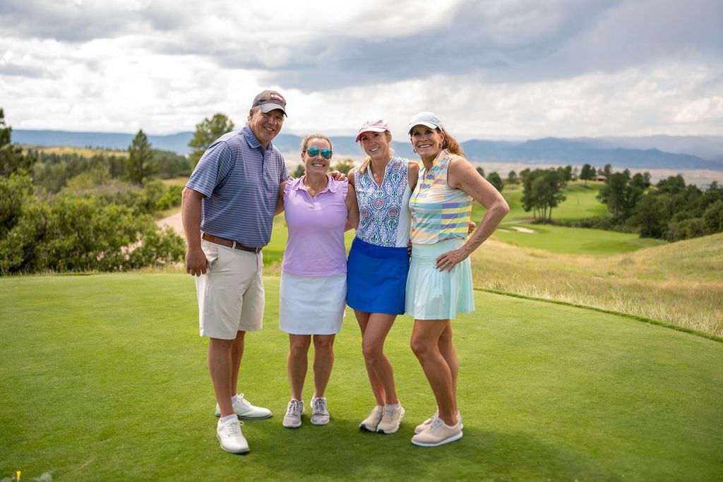 One male and three female golfers smiling together on the tee box.