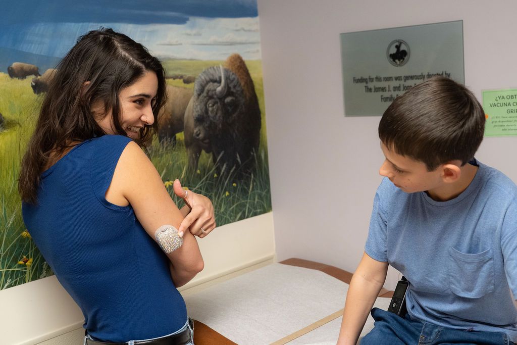 Female medical worker showing young boy how to put on his CGM device.