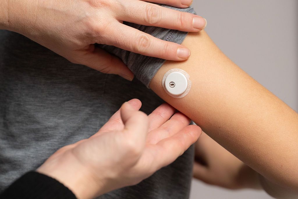 Two young girls showing each other their CGM devices the back of on their arms.