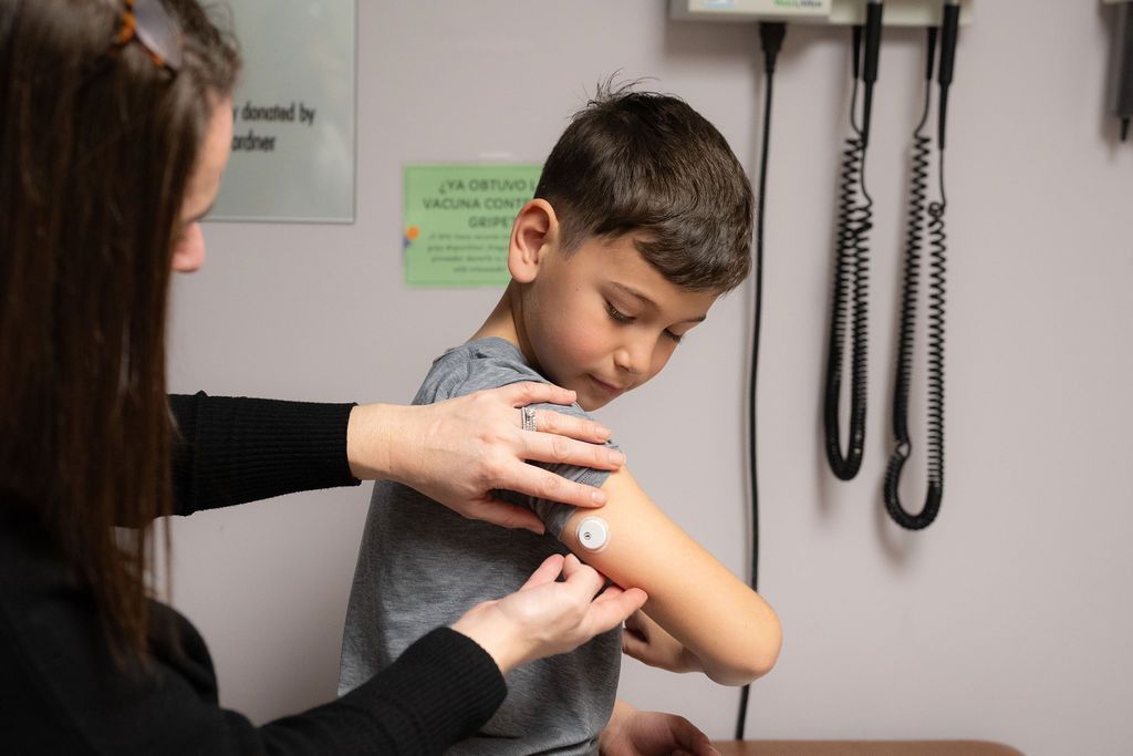 Female medical worker showing young boy how to put on his CGM.