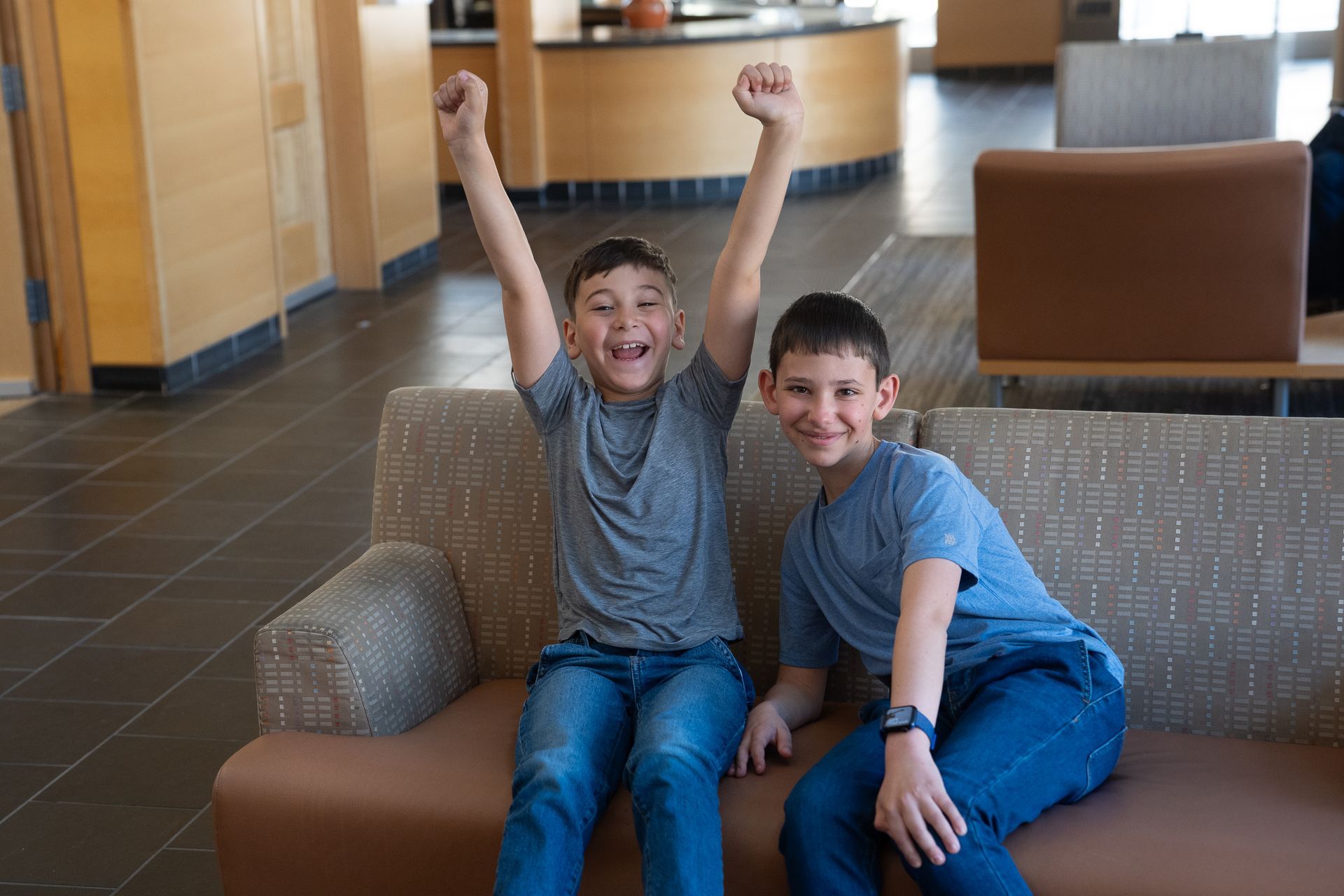 Two smiling T1D advocate boys smiling together on a couch with one boy's hands raised.