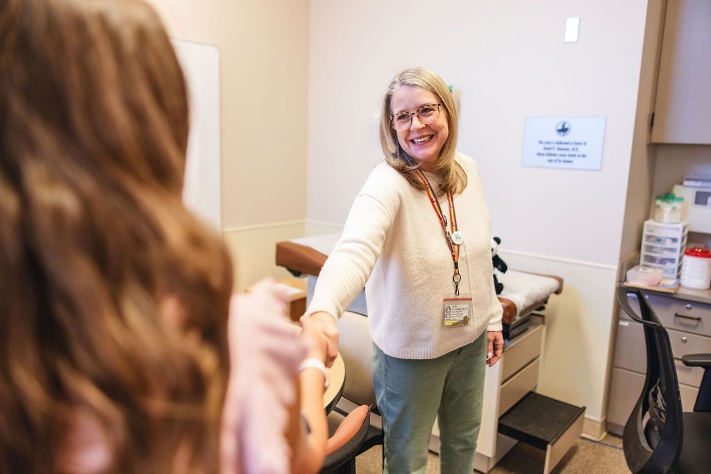 Smiling female social worker shaking the hand of a patient in an exam room.