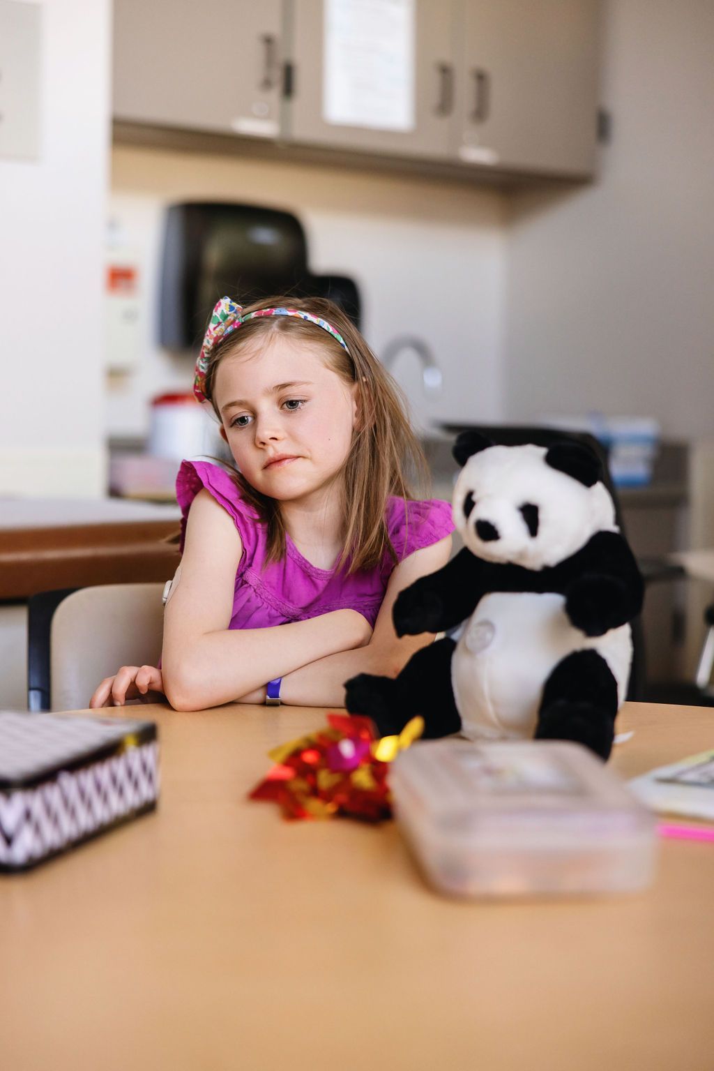 Young girl with CGM on her arm sitting at a table looking sad.