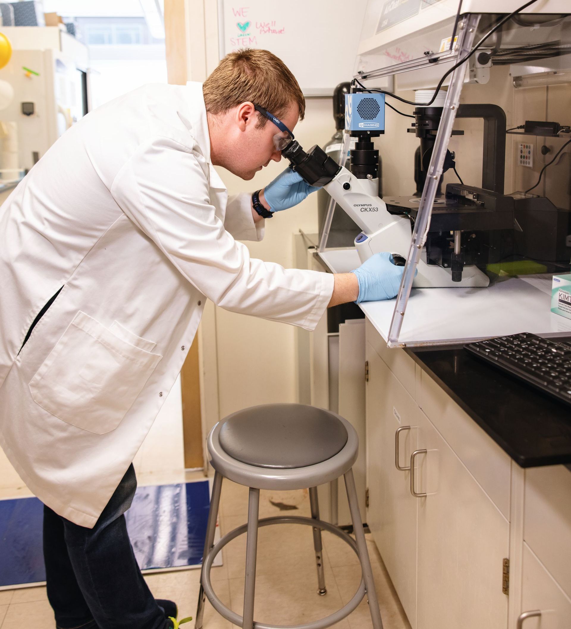 Male researcher in white lab coat looking through a microscope.