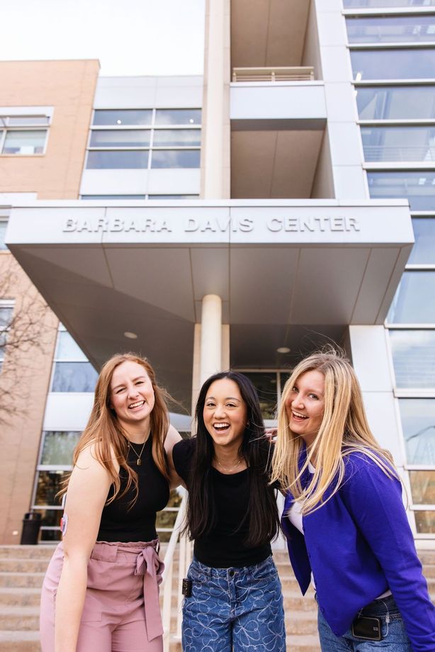 Three women laughing while standing outside of the Barbara Davis Center.