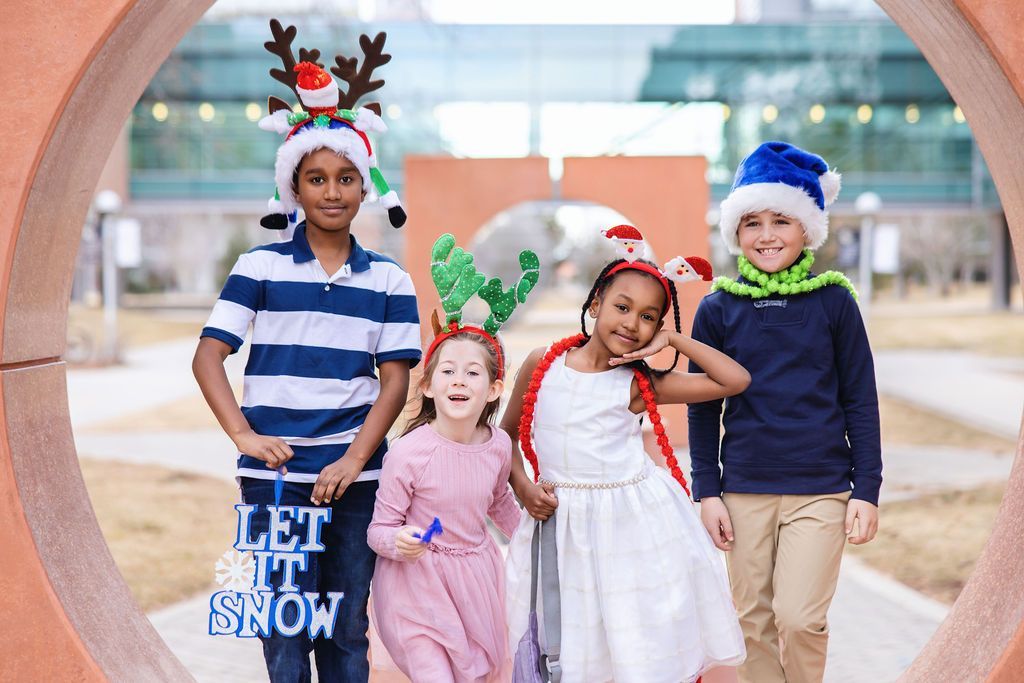 Group of four kids posing in antlers and holiday hats.