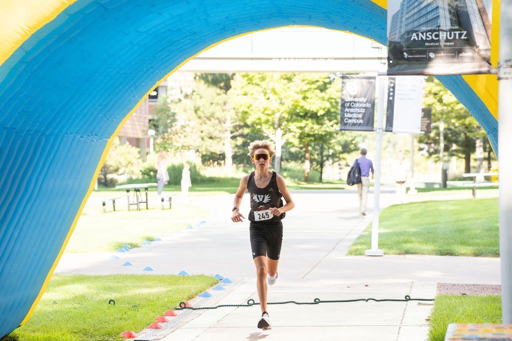 teen boy running through inflatable arch in sunglasses and race bib