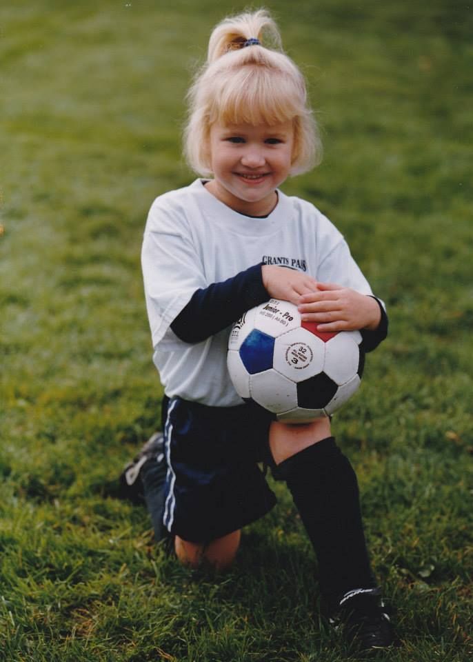 A young girl is kneeling down holding a soccer ball