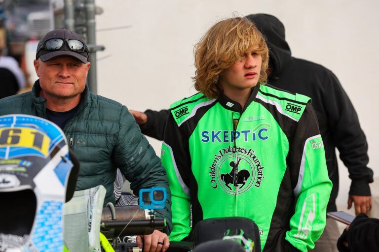 A man standing next to a boy wearing a green jacket that says skeptic