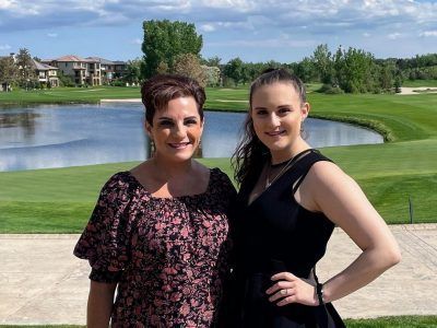 Two women are standing next to each other in front of a golf course.