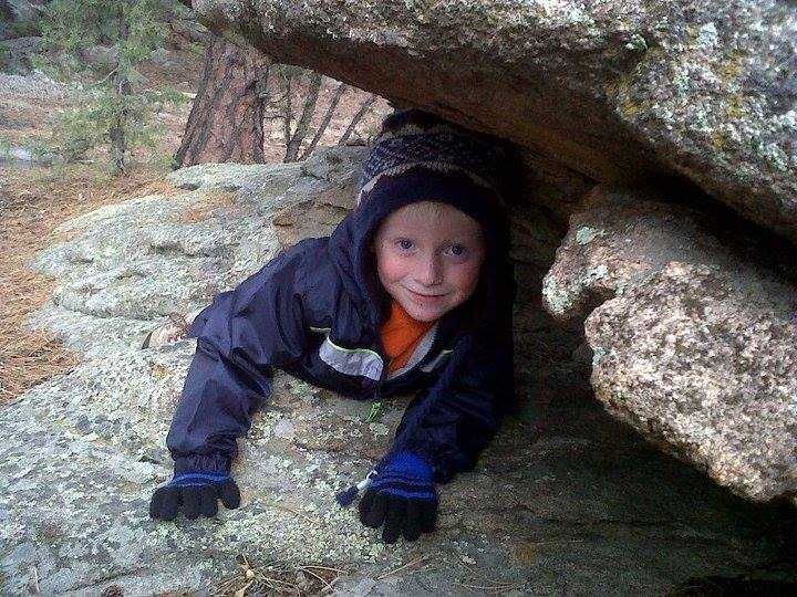 A young boy is crawling under a large rock