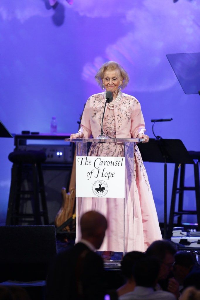 A woman in a pink dress is giving a speech at a podium