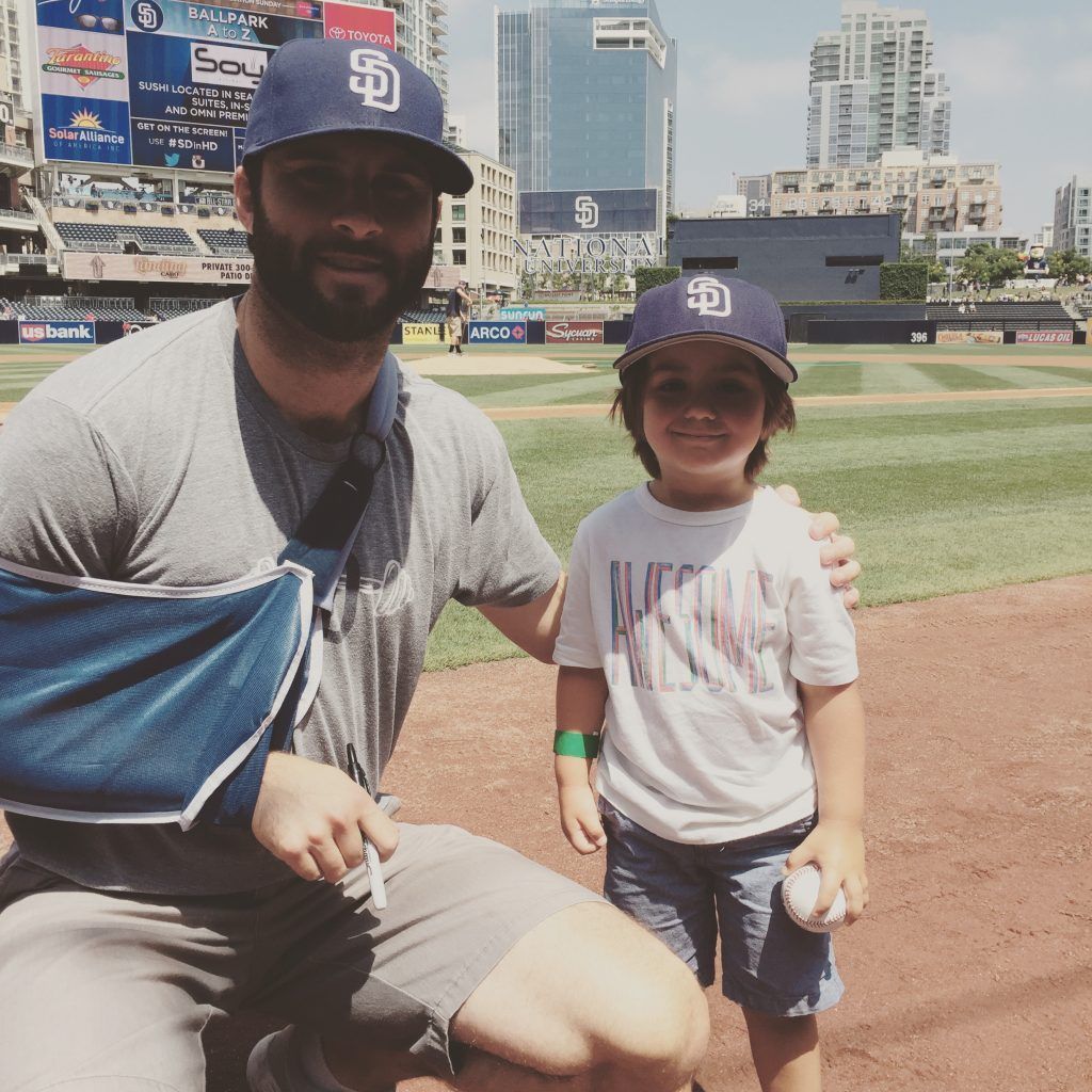 A man with a broken arm is posing for a picture with a little boy wearing a san diego padres hat