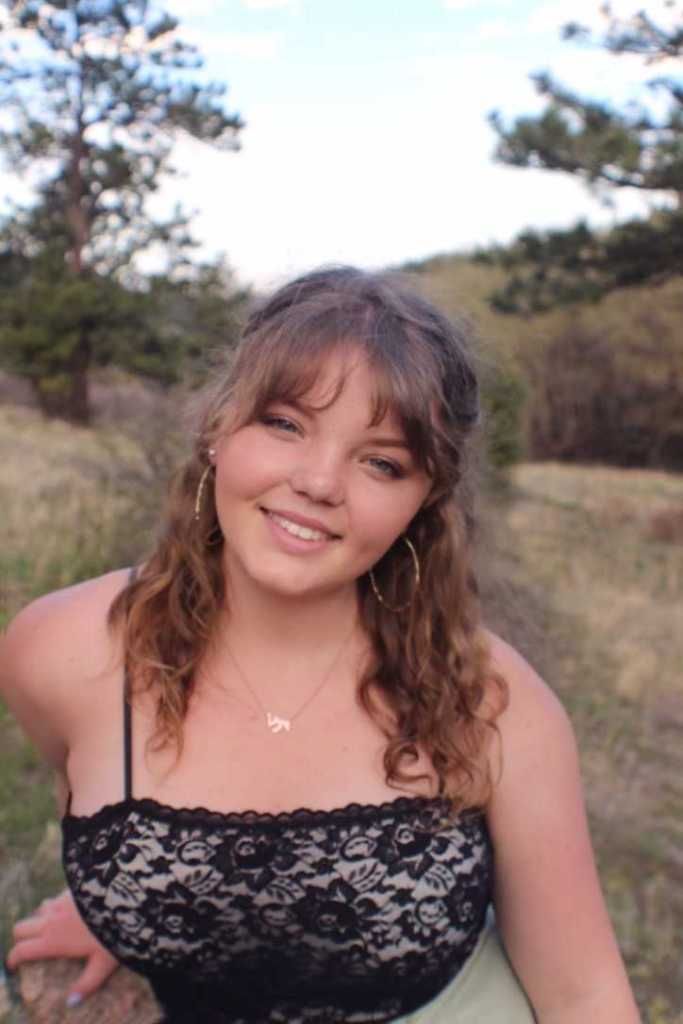 A woman in a black lace top is standing in a field.