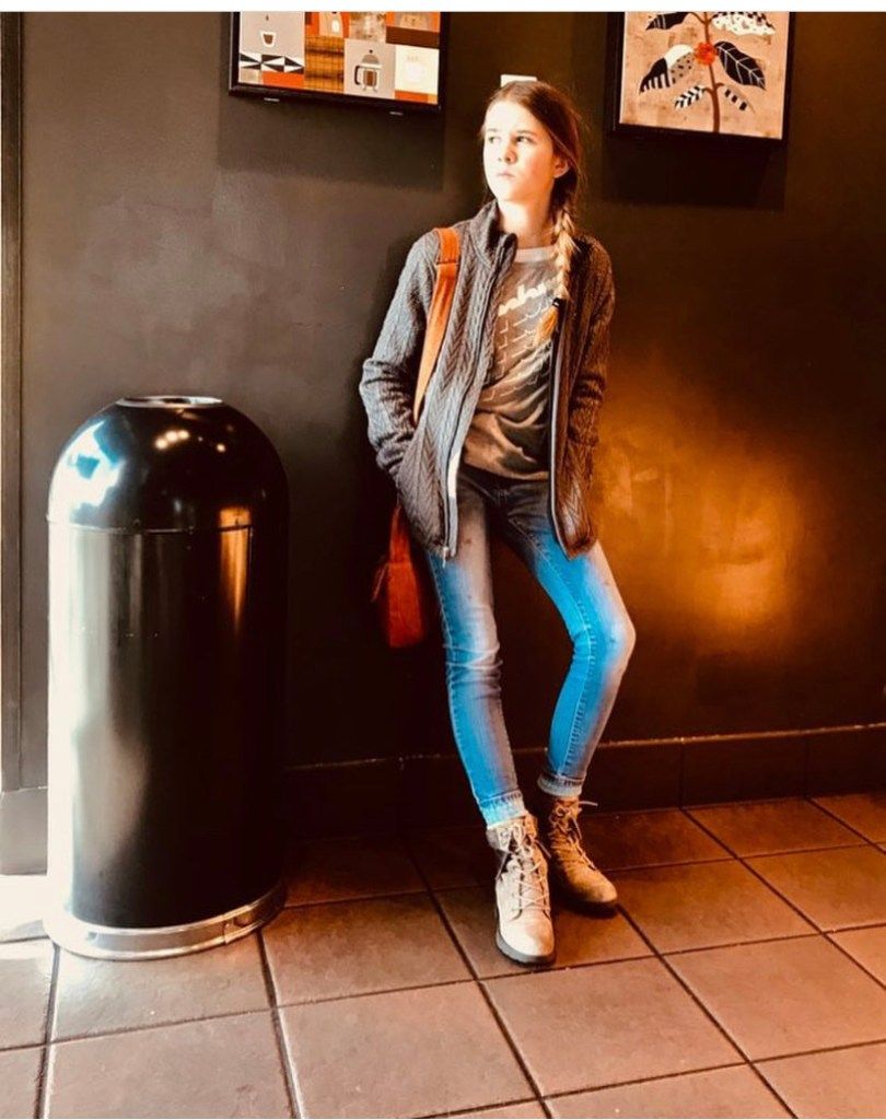 A girl leaning against a wall next to a trash can