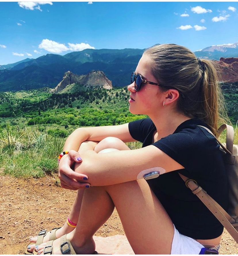 A woman with a patch on her arm sits in front of a mountain range