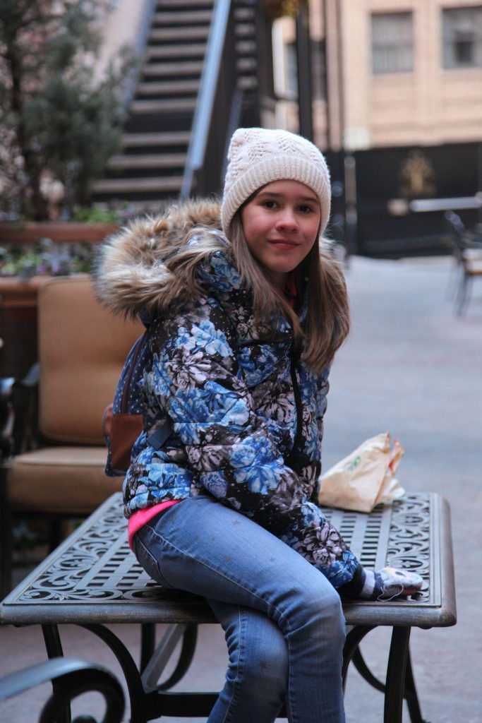 A young girl is sitting on a bench with a sandwich in her hand.