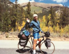 A man standing next to a bicycle with a mountain in the background
