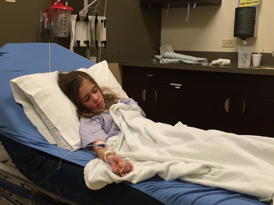 A young girl is laying in a hospital bed with an iv in her arm