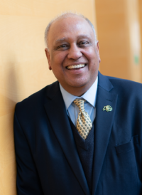 A man in a suit and tie is smiling and leaning against a wall