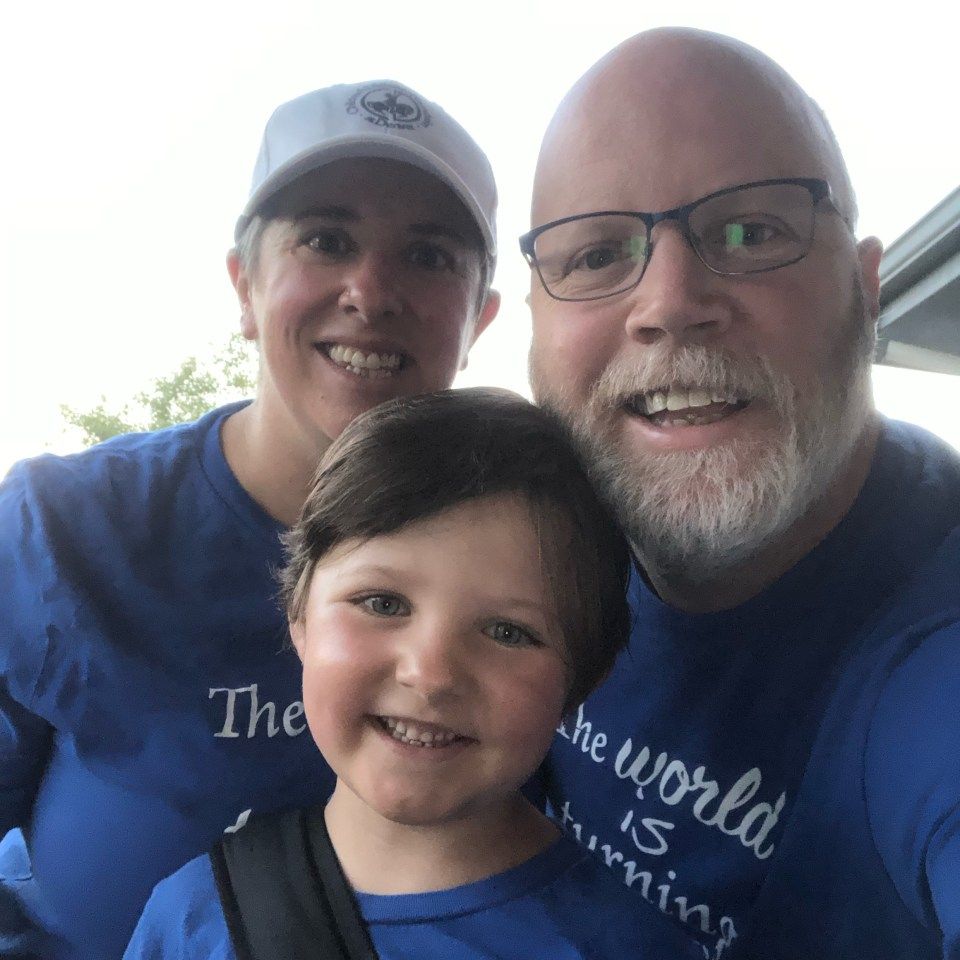 A man and woman are posing for a picture with a child wearing a shirt that says the world is shrinking