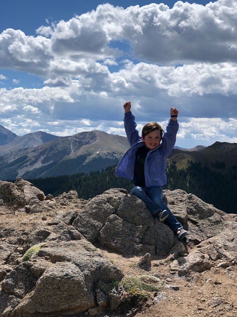 A young boy is sitting on a rock with his arms in the air.