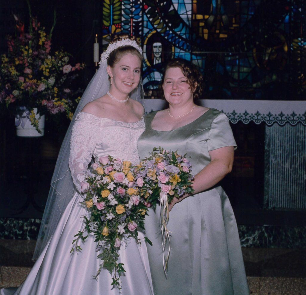 A bride and her bridesmaid pose in front of a stained glass window