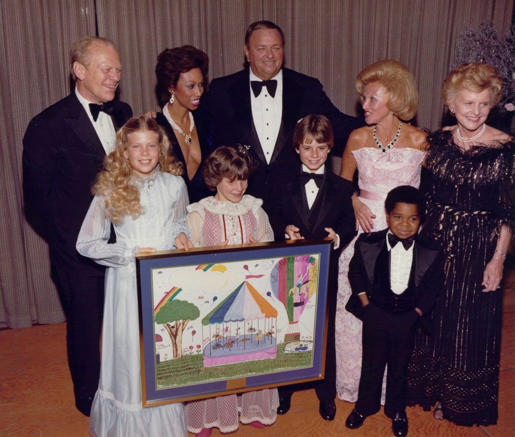A group of people posing for a picture with a framed picture of a carnival