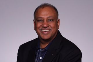 A man in a black jacket and blue shirt is smiling for the camera.