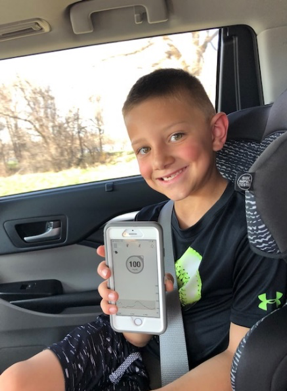 A young boy is sitting in the back seat of a car holding a cell phone
