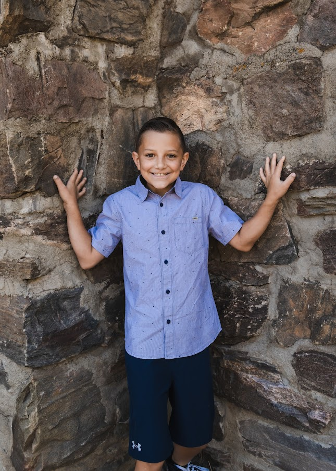 A young boy is standing in front of a stone wall.