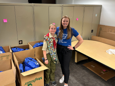 Two girl scouts are standing next to each other in a room filled with boxes.
