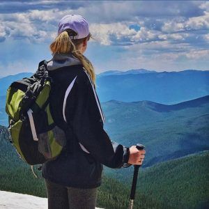 A woman with a backpack and hiking poles looks out over a mountain range