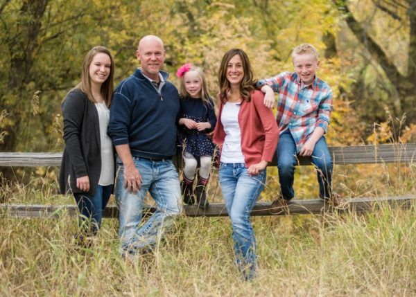 A family is posing for a picture while sitting on a wooden fence in a field.