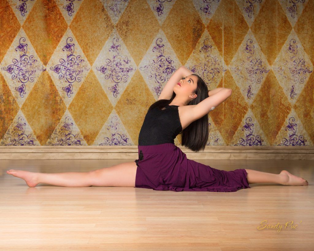 A woman in a purple skirt is doing a split on a wooden floor.