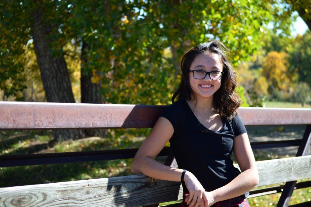 A young woman is sitting on a wooden bench in a park.