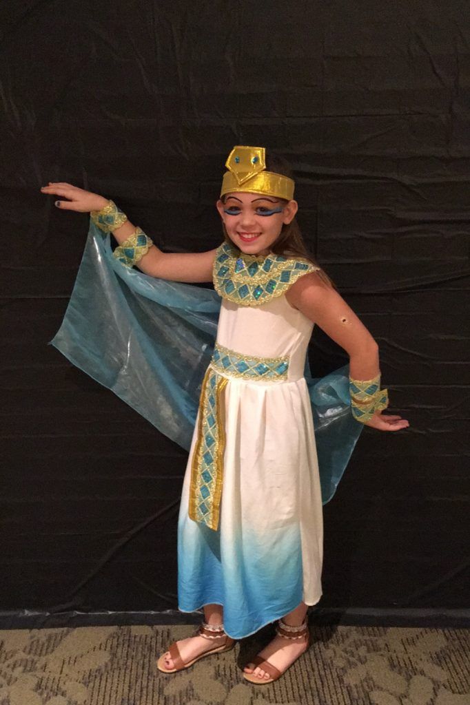 A little girl in a costume of a pharaoh is standing in front of a black wall.