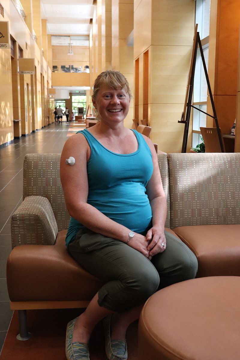 A pregnant woman is sitting on a couch with a patch on her arm.