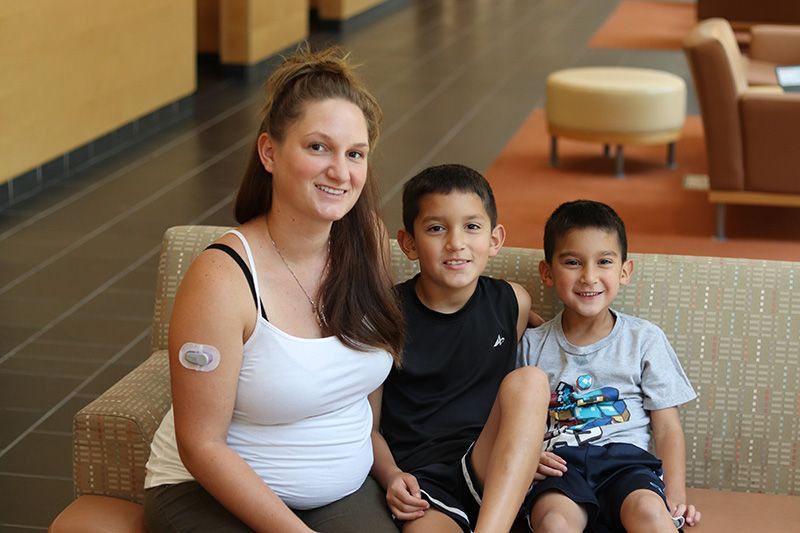 A pregnant woman is sitting on a couch with two children.