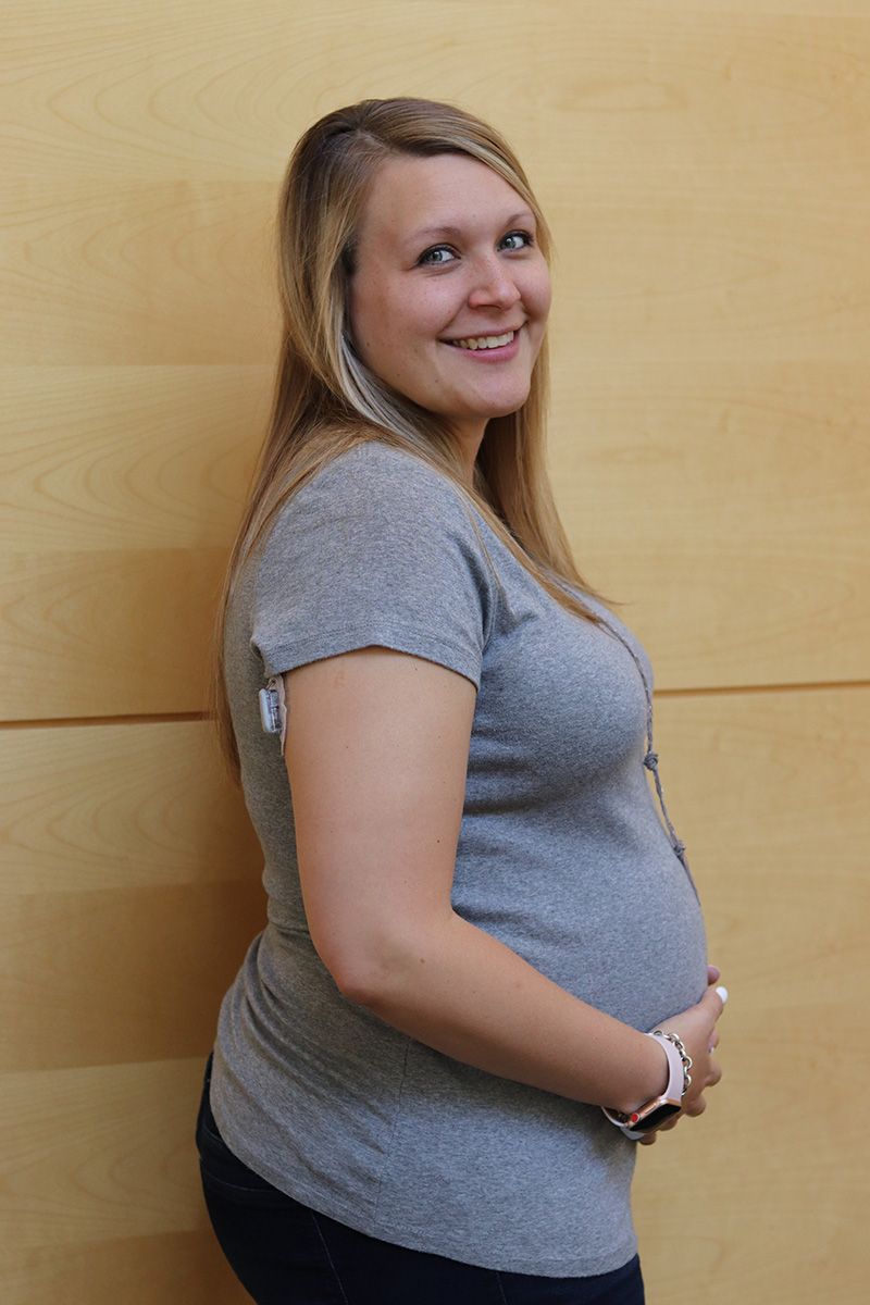 A pregnant woman in a grey shirt is smiling and holding her belly