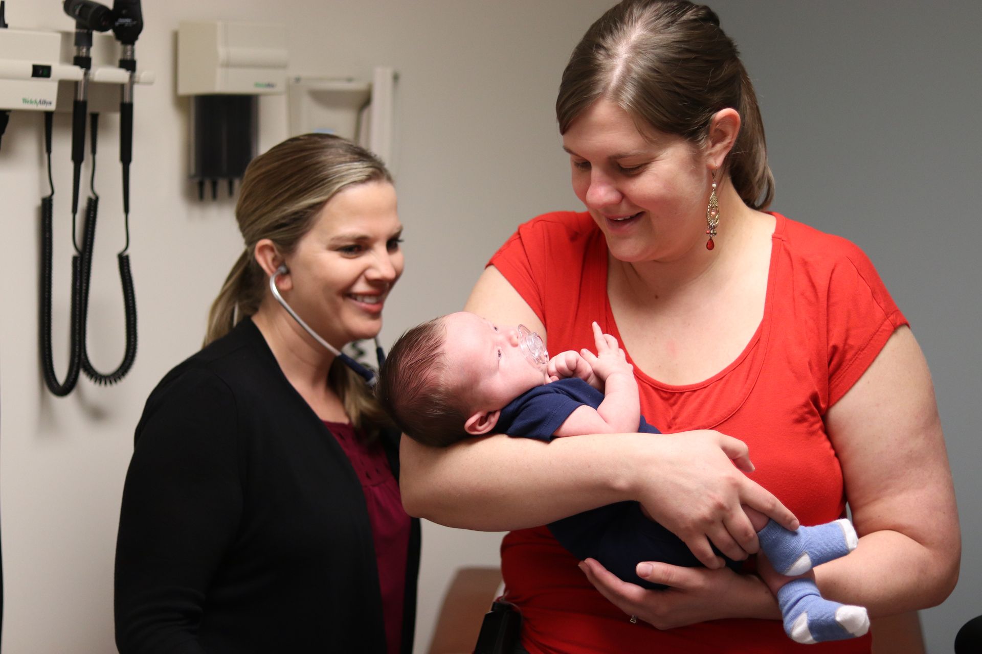 Smiling T1D mother holding her newborn baby while being examined by doctor at the BDC.
